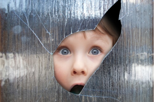 Young boy looking through a smashed window